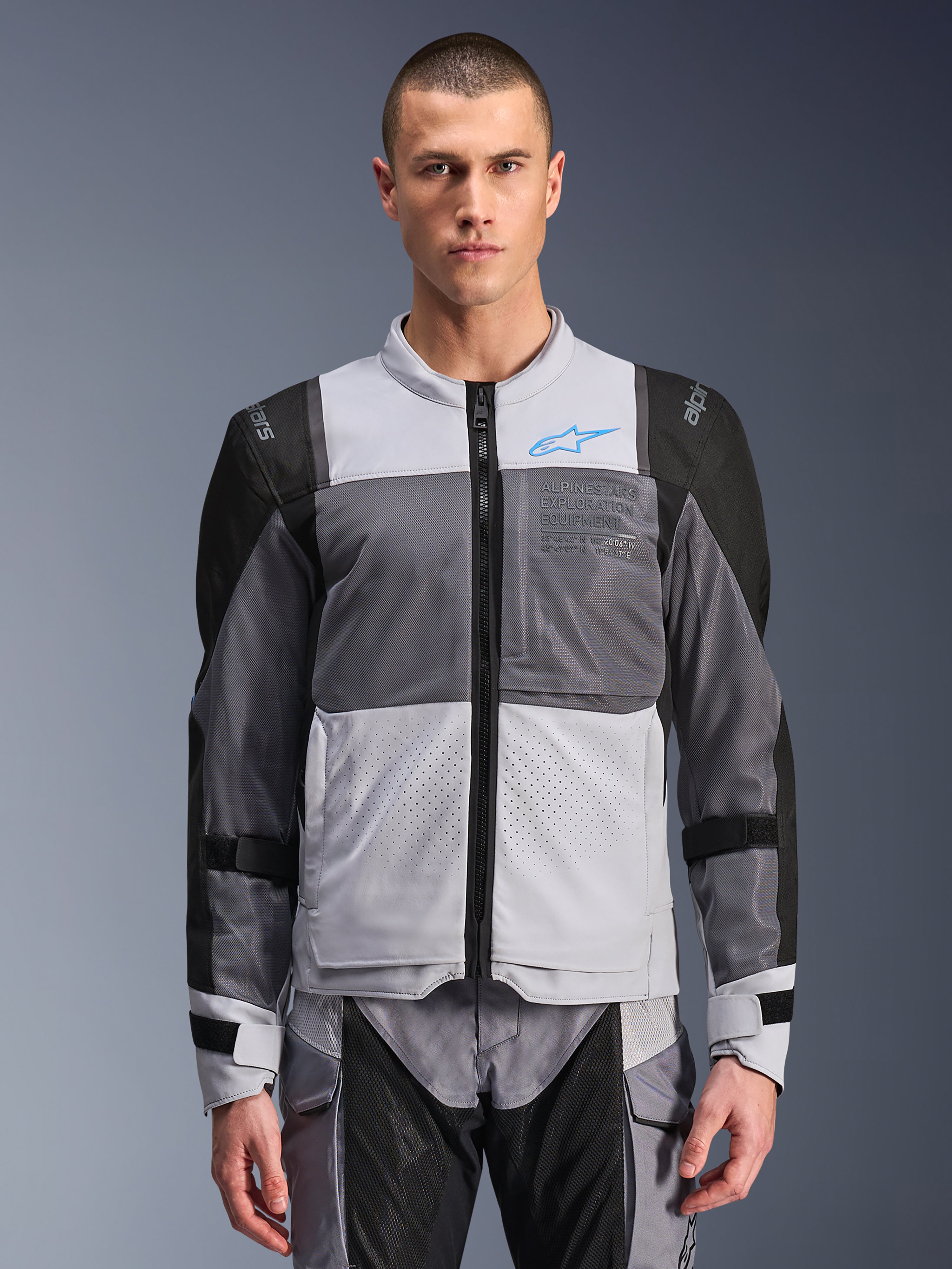 Alpinestars ST-2 Air Jacket, motorcykeljakke til herrer, Ice Gray og Dark Gray med sorte detaljer, brede mesh-ventilationspaneler, laserperforeret front, blåt Alpinestars-logo, lynlås foran, båret af en model med matchende kørebukser