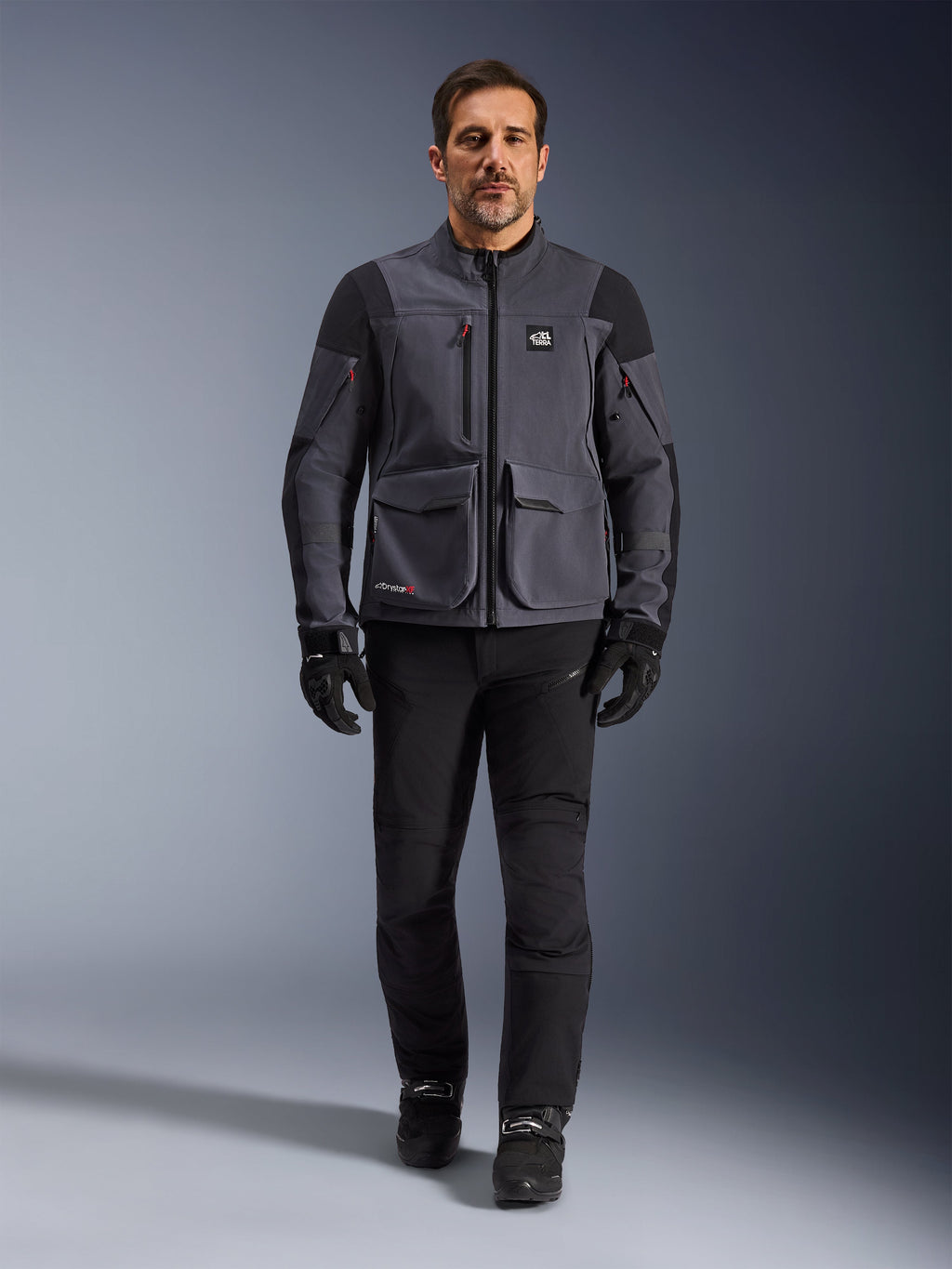 Maxdura Drystar®XF Laminated Armored Shell, motorcykeljakke, Deep Gray Black, båret af en model med sorte bukser og handsker, med store cargo-lommer, røde lynlåsdetaljer og All Terra-branding, teknisk adventure-køreudstyr