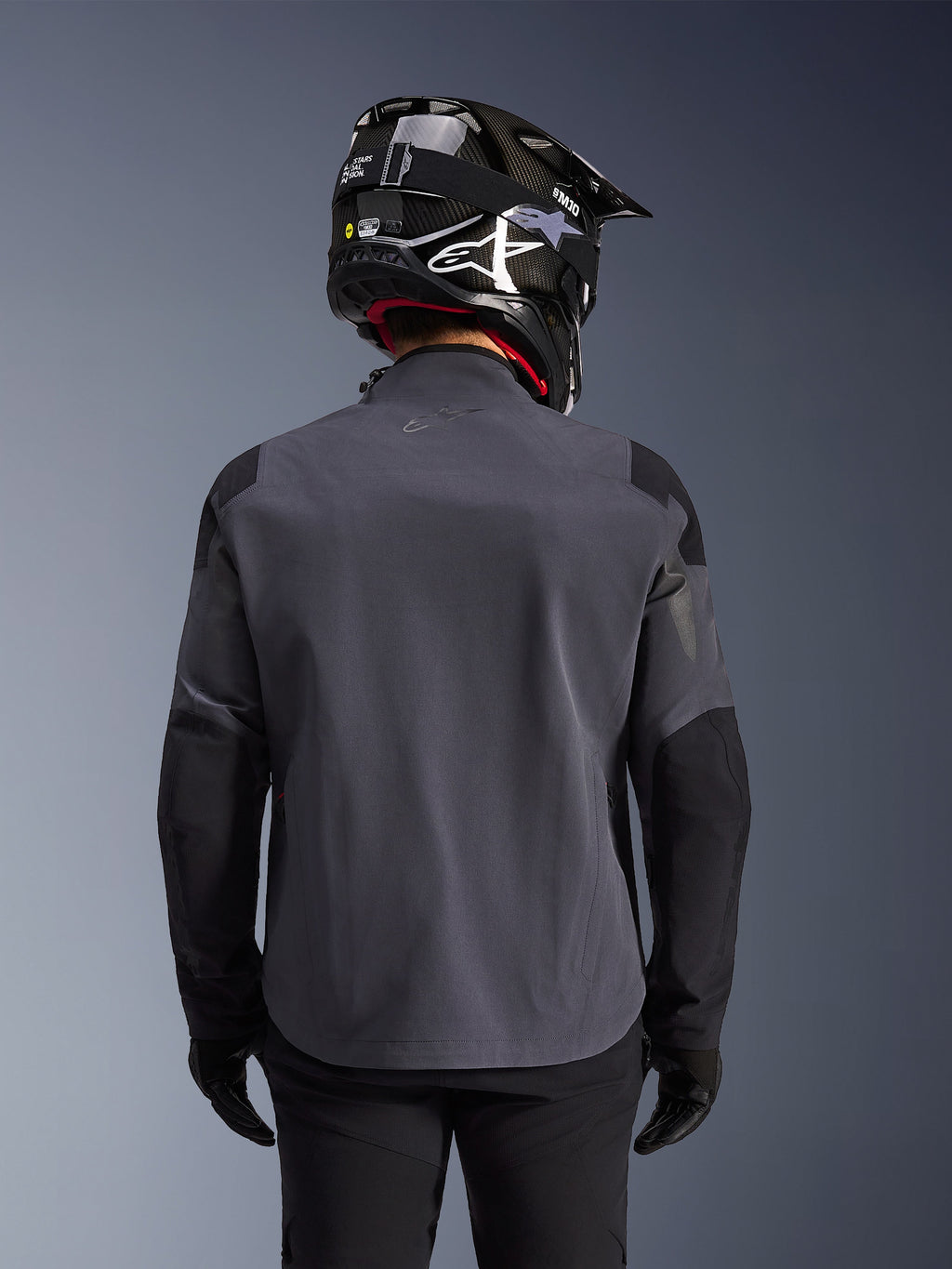 Alpinestars Maxdura Drystar®XF Laminated Armored Shell, adventure motorcykeljakke, Deep Gray Black, set bagfra med fokus på den tekniske tekstilkonstruktion og forstærkede paneler, båret med sort kulfiberhjelm, sorte kørebukser og handsker