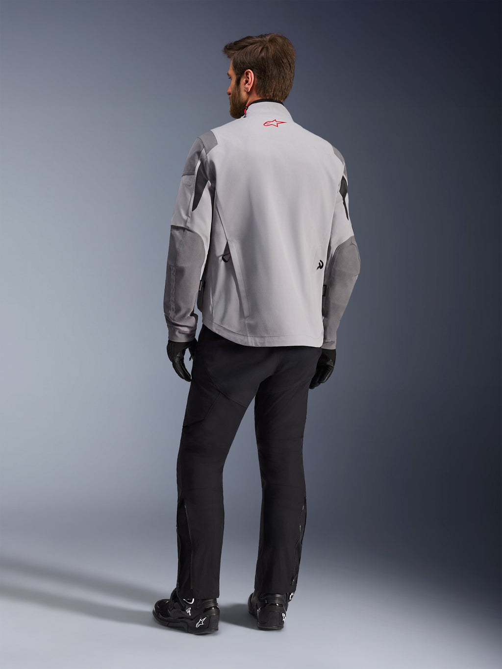 Maxdura Drystar®XF Lamineret Armored Shell, motorcykeljakke, mellemgrå og mørkegrå, set bagfra med rødt Alpinestars-logo på kraven, mørkegrå ærmeforstærkninger, båret med sorte bukser og støvler, adventure-køreudstyr