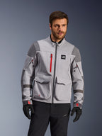 Alpinestars Maxdura Drystar®XF lamineret adventure motorcykeljakke, mellemgrå og mørkegrå med røde detaljer, bæres af en model med sorte handsker og bukser, med store cargo-lommer og vandtætte lynlåse, professionelt køreudstyr