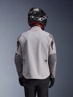 Alpinestars Maxdura Drystar®XF Laminated Armored Shell, adventure motorcykeljakke, mellemgrå og mørkegrå, set bagfra med lysegrå krop og mørkere grå forstærkede paneler på skuldre og albuer, rødt Alpinestars-logo på øverste del af ryggen, båret med sort hjelm og sorte handsker.