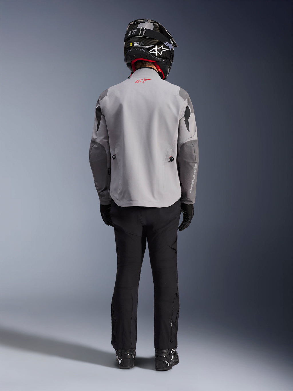 Alpinestars Maxdura Drystar®XF Laminated Armored Shell, motorcykeljakke i Mid Gray og Dark Gray, set bagfra på en rytter, båret med sorte bukser, sorte støvler og en sort og hvid hjelm, adventure touring-udstyr