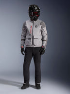Alpinestars Maxdura Drystar®XF Lamineret Armored Shell, mellemgrå og mørkegrå adventure-jakke med røde lynlåsdetaljer, båret af en kører med en sort hjelm, røde briller og sorte bukser, professionelt motorcykeludstyr til al slags vejr