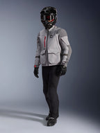Adventure-rytter iført Alpinestars Maxdura Drystar®XF lamineret motorcykeljakke i mellemgrå og mørkegrå, sort adventure-hjelm med crossbriller, sorte bukser og handsker, med røde lynlåsdetaljer og cargo-lommer, teknisk udstyr til adventure touring.