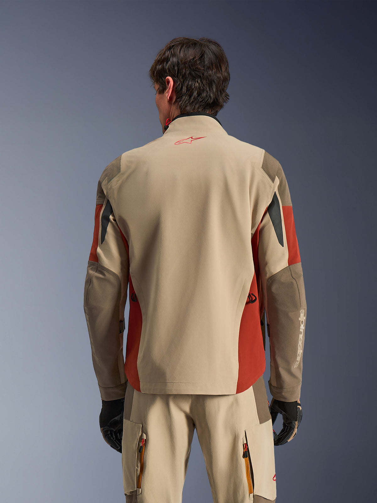 Mand iført Alpinestars Maxdura Drystar®XF Laminated Armored Shell set bagfra, adventure-jakke i Aluminum Walnut og Rust Brown, matchende tekniske bukser og sorte handsker, 3-lags lamineret tekstilkonstruktion med forstærkede paneler, koordineret outfit til motorcykel-touring