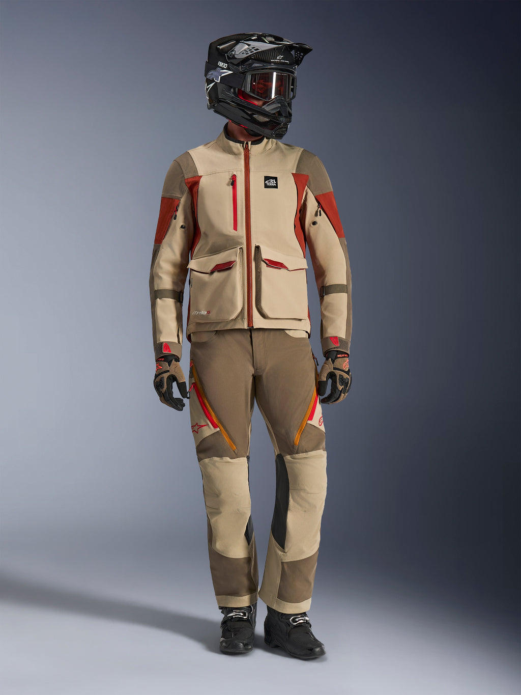 Helkropsstudiebillede af en rytter iført Alpinestars Maxdura Drystar®XF Laminated Armored Shell-jakke i Aluminum Walnut Rust Brown, kombineret med matchende adventure-bukser, en sort off-road hjelm med rødfarvede goggles og tekniske handsker, der viser et komplet adventure touring-sæt.