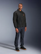 Alpinestars Revved WR-jakke i sort, urban motorcykeljakke i coach-stil, båret af en model med mørkeblå jeans og sorte sneakers, med trykknapper foran og broderet logo, minimalistisk og sporty design til landevejskørsel.