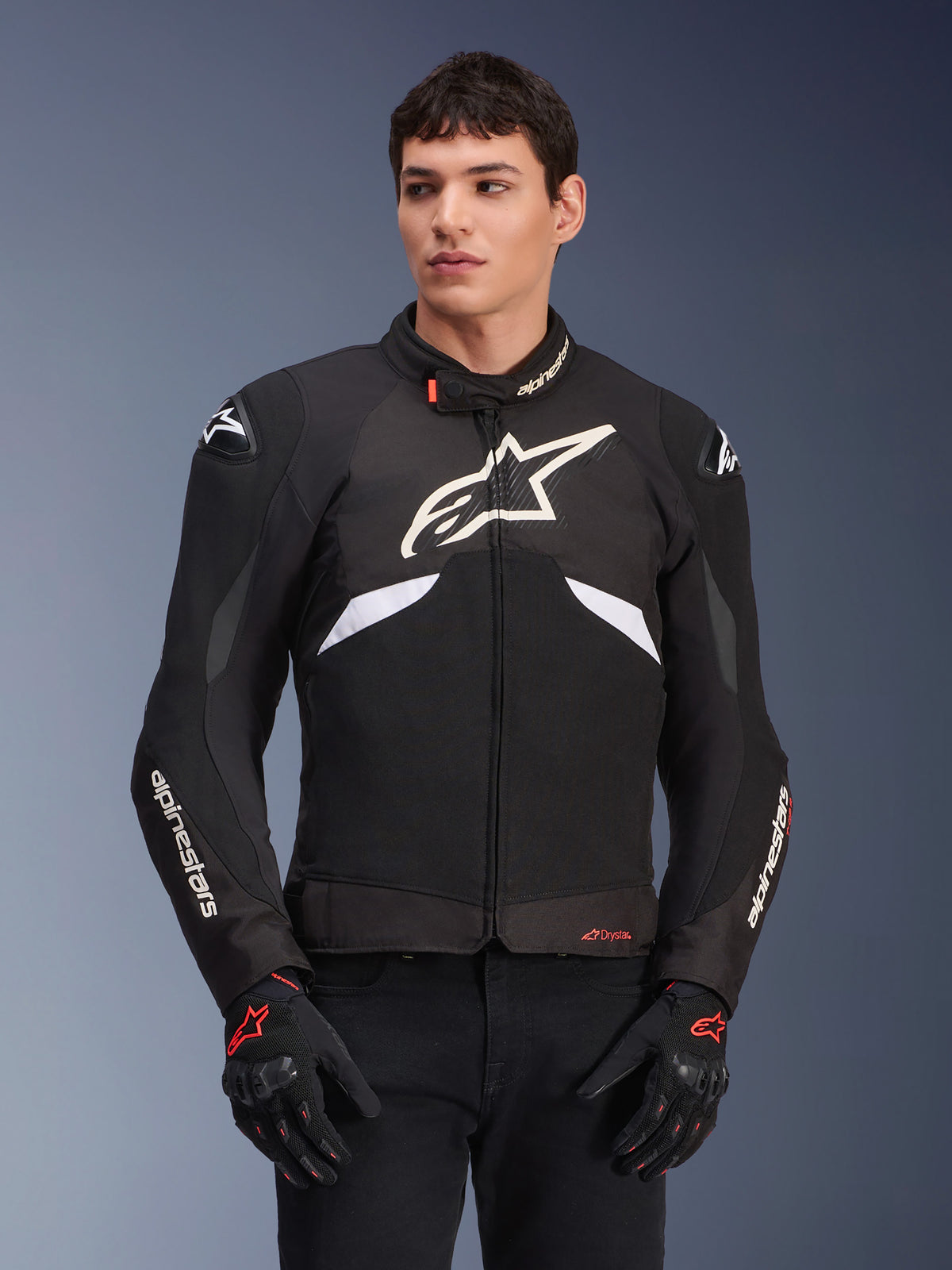 Alpinestars T-GP R V3 Drystar jakke, vandtæt sportstekstiljakke, sort og hvid med røde detaljer, stort hvidt stjernelogo på brystet, hvid branding på ærmerne, båret med sorte og røde motorcykelhandsker