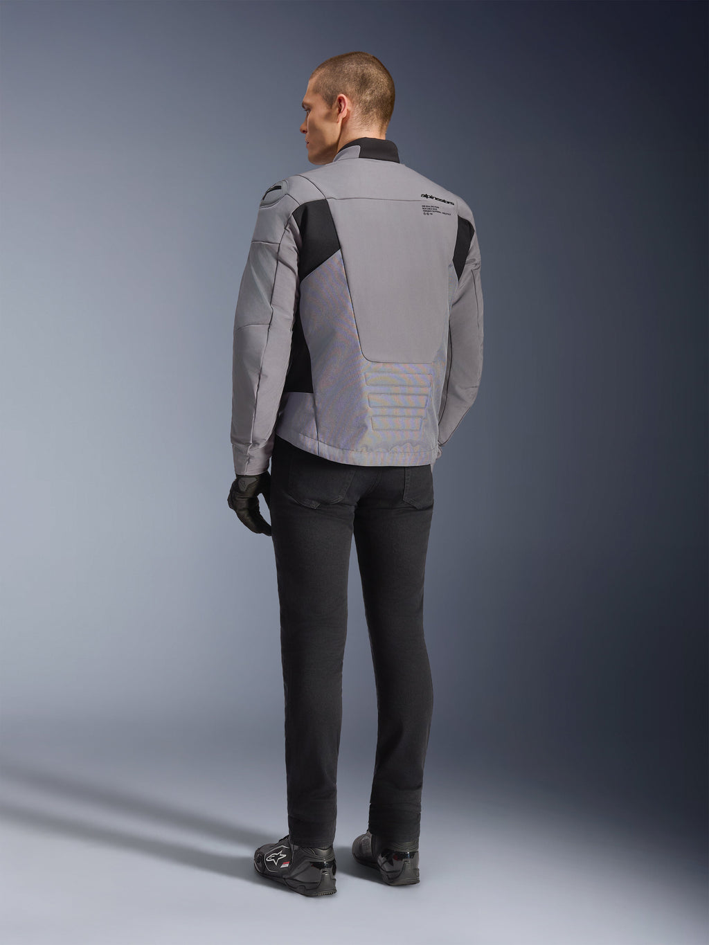 Alpinestars SMX vandtæt jakke i mørkegrå og sort, set bagfra på en model, båret med sorte bukser og støvler, teknisk tekstilkonstruktion med sorte paneler og Alpinestars-branding på skulderen.