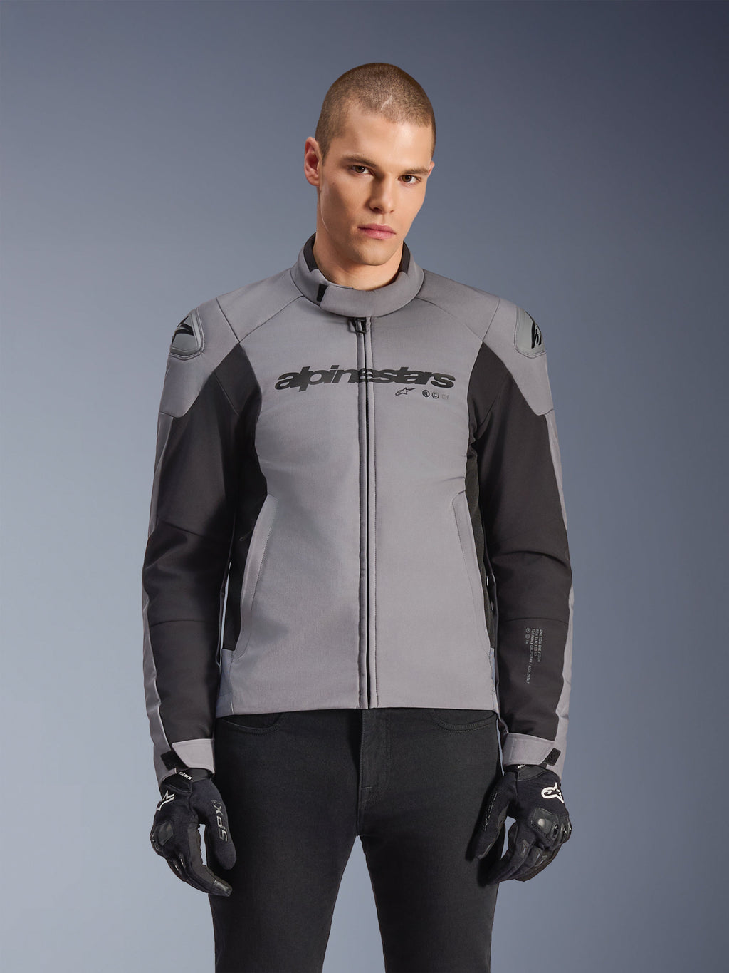 Alpinestars SMX Waterproof Jacket, sportslig motorcykeljakke til vejbrug, mørkegrå og sort, med høj krave og DFS Lite-skulderbeskyttere, båret med sorte SMX-handsker, slank atletisk pasform til kørsel i al slags vejr