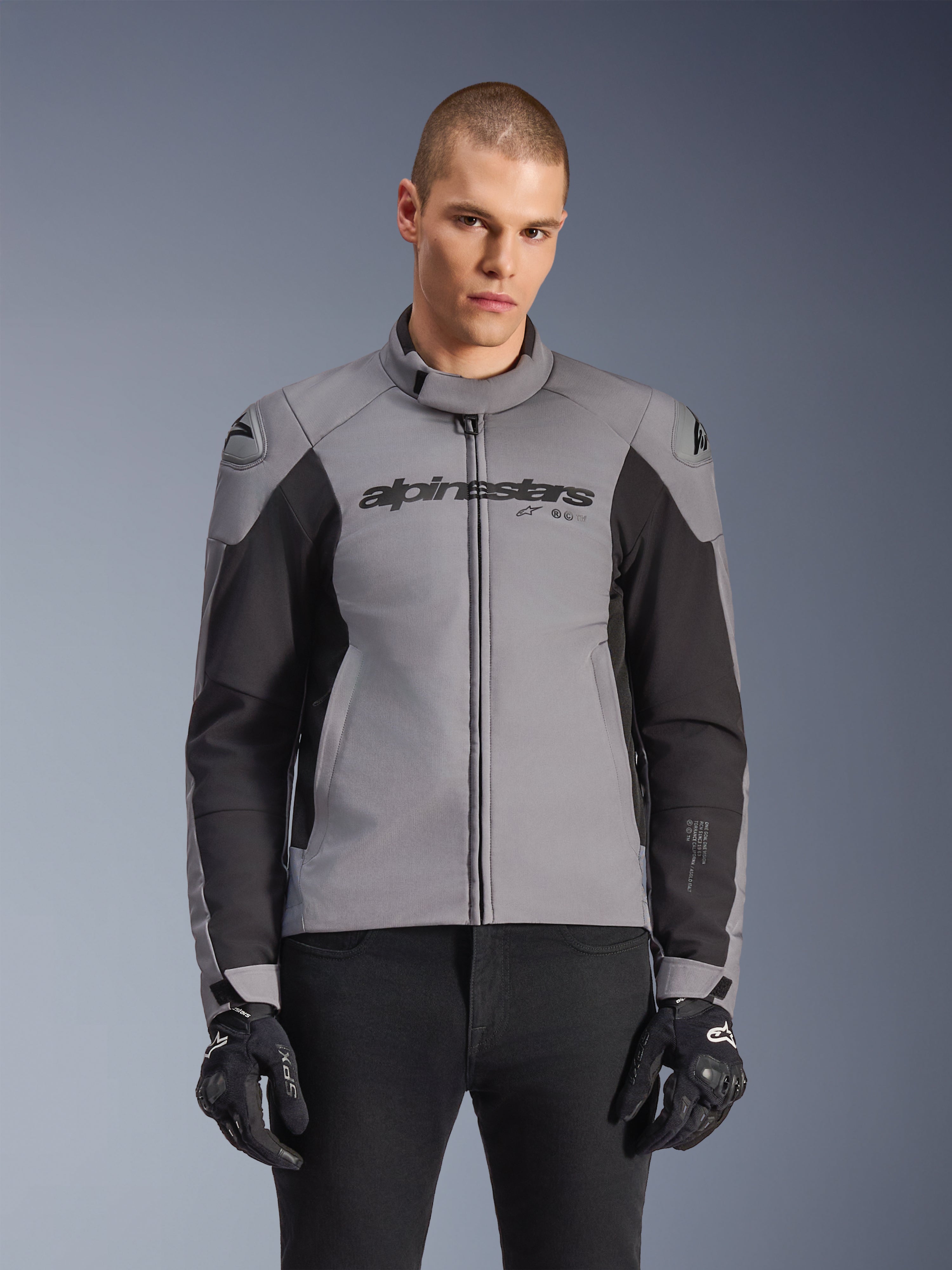 Alpinestars SMX Waterproof Jacket, sportslig motorcykeljakke til vejbrug, mørkegrå og sort, med høj krave og DFS Lite-skulderbeskyttere, båret med sorte SMX-handsker, slank atletisk pasform til kørsel i al slags vejr