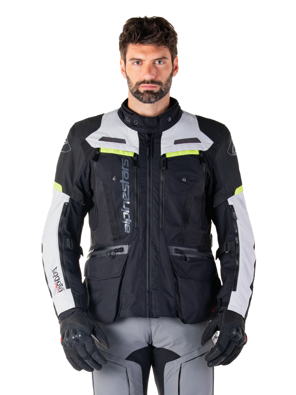 Mand iført Alpinestars Bogotá Pro Drystar-jakke, sort og lysegrå med neongule detaljer, helårs adventure touring motorcykeljakke, vandtæt design med flere lommer og lodret branding, kombineret med sorte handsker og grå kørebukser