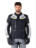 Mand iført Alpinestars Bogotá Pro Drystar-jakke, sort og lysegrå med neongule detaljer, helårs adventure touring motorcykeljakke, vandtæt design med flere lommer og lodret branding, kombineret med sorte handsker og grå kørebukser