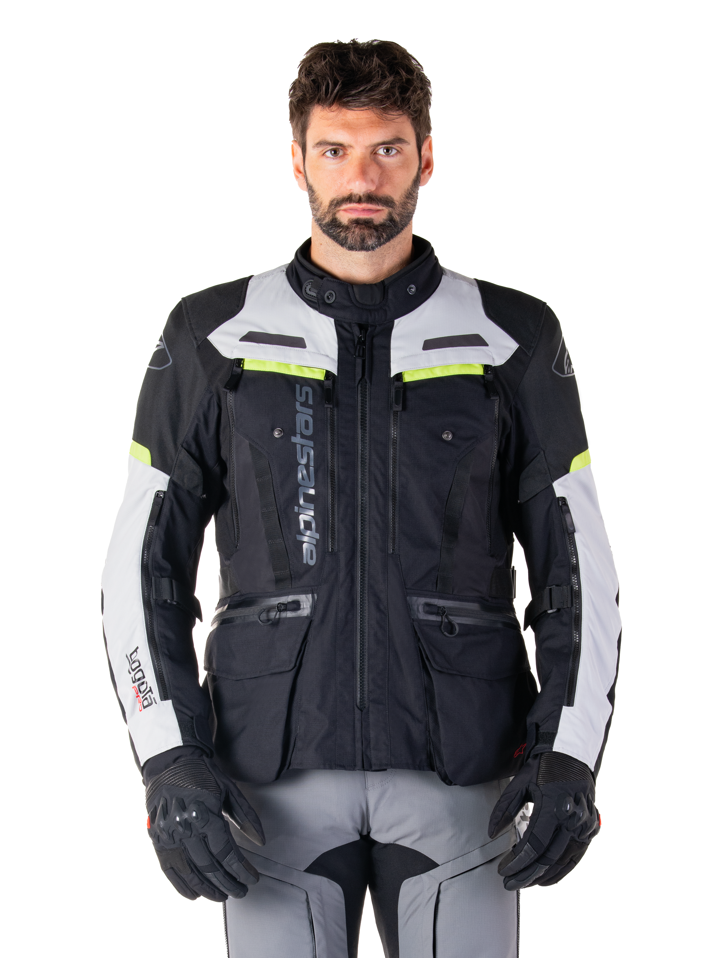 Mand iført Alpinestars Bogotá Pro Drystar-jakke, sort og lysegrå med neongule detaljer, helårs adventure touring motorcykeljakke, vandtæt design med flere lommer og lodret branding, kombineret med sorte handsker og grå kørebukser