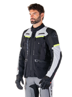 Alpinestars Bogotá Pro Drystar®-jakke, adventure touring-motorcykeljakke, Black Ice Gray og Yellow Fluo, båret af en mand med matchende grå bukser og sorte handsker, med tekniske ventilationspaneler og design med flere lommer.