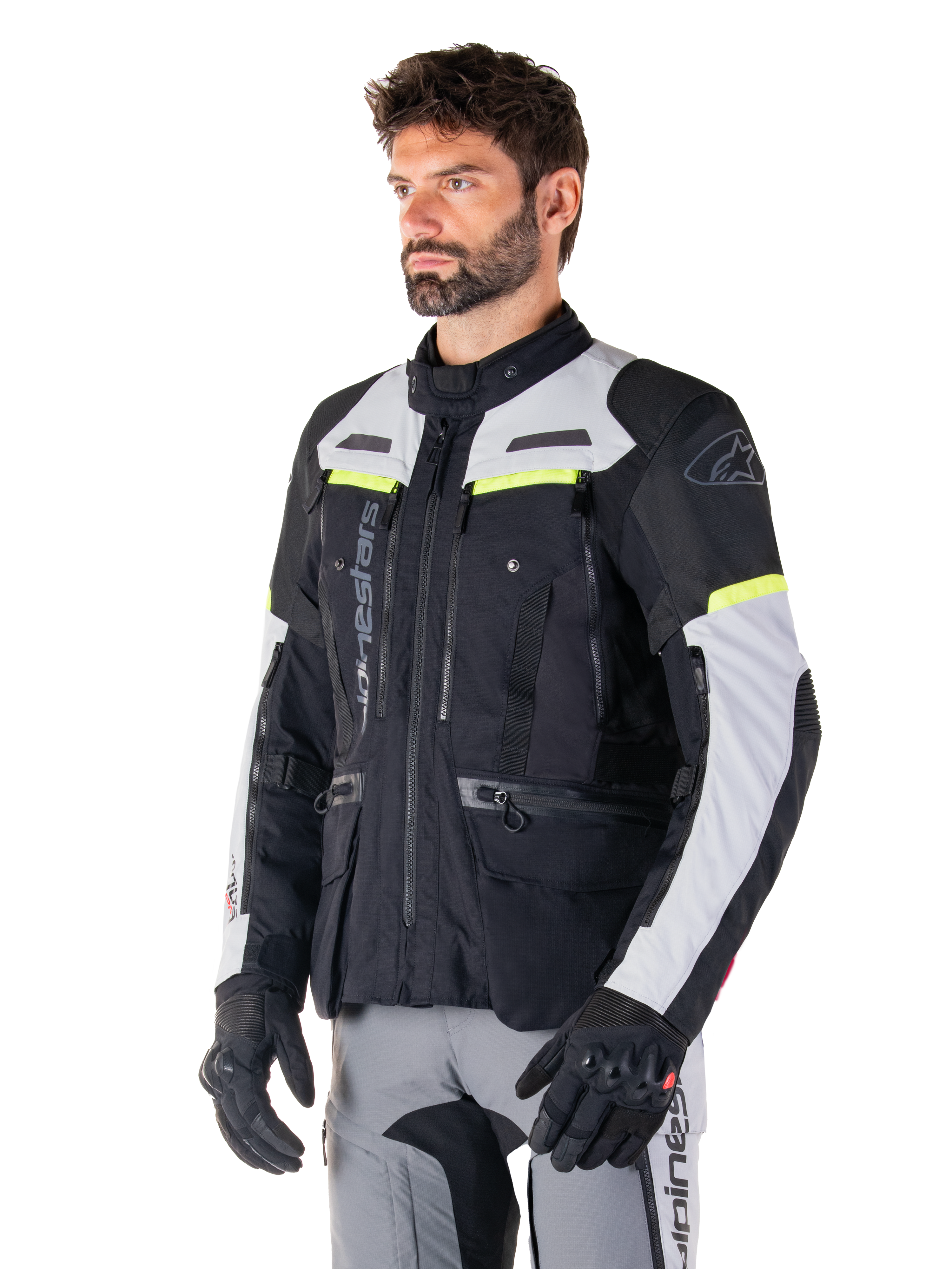 Alpinestars Bogotá Pro Drystar®-jakke, adventure touring-motorcykeljakke, Black Ice Gray og Yellow Fluo, båret af en mand med matchende grå bukser og sorte handsker, med tekniske ventilationspaneler og design med flere lommer.