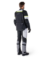 Bagfra set af en motorcyklist iført Alpinestars Bogotá Pro Drystar®-jakke i Black Ice Gray Yellow Fluo, kombineret med matchende adventure touring-bukser, med en stor baglomme og gule fluorescerende detaljer, helårs tekstil motorcykeludstyr.