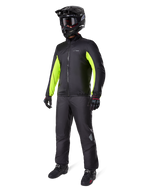Motorcyklist iført Alpinestars Bogotá Pro Drystar®-jakkeliner, sort med klare Yellow Fluo-paneler på ærmerne, matchende sorte bukser, sort motocrosshjelm og handsker, vandtæt helårs-adventure-udstyr