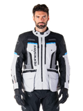 Alpinestars Bogota Pro Drystar jakke, adventure touring-motorcykeljakke, Ice Gray med sorte og cyanblå detaljer, set forfra med ventilationspaneler og cargolommer, båret af en model med sorte kørebukser og handsker