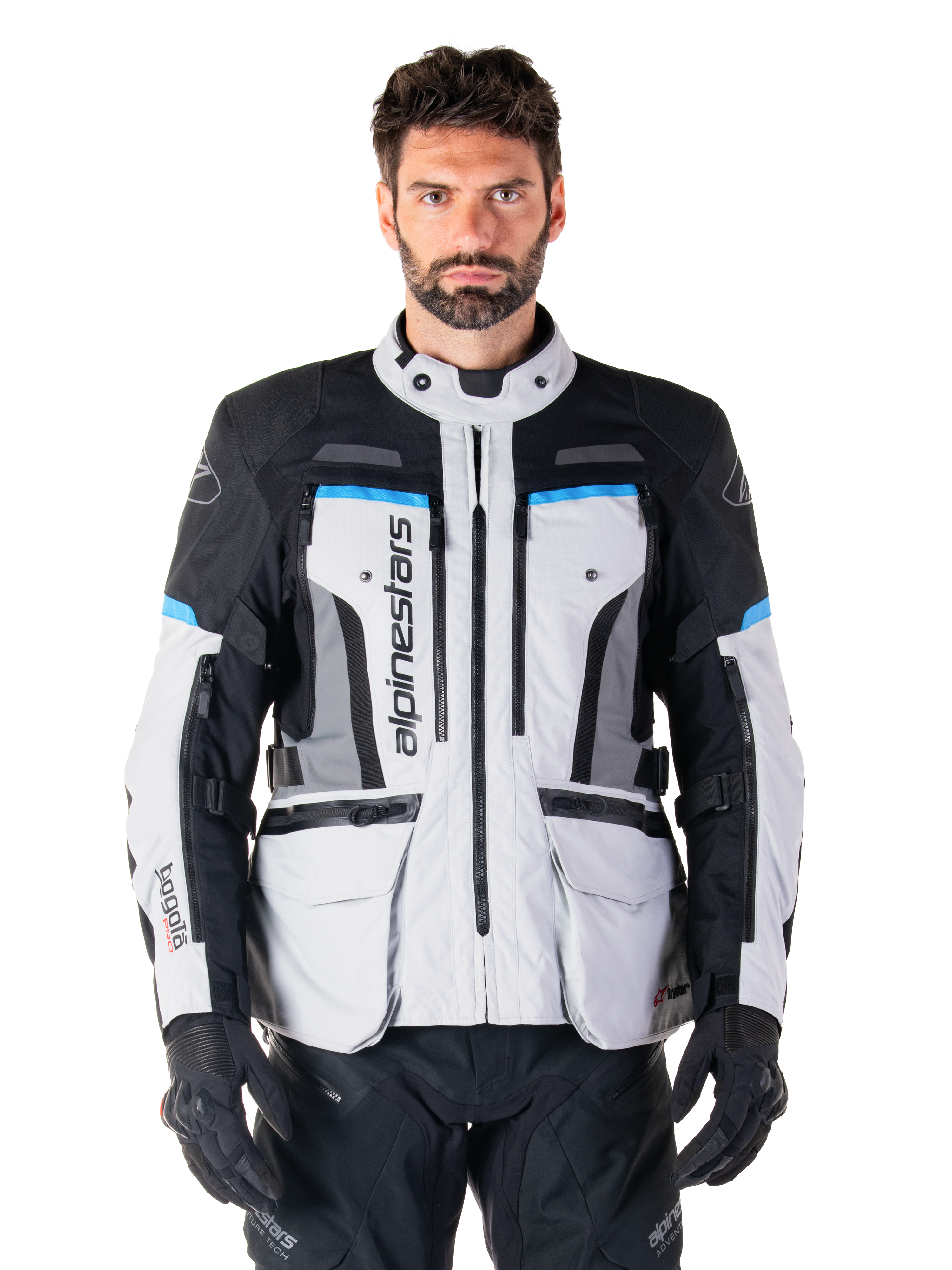 Alpinestars Bogota Pro Drystar jakke, adventure touring-motorcykeljakke, Ice Gray med sorte og cyanblå detaljer, set forfra med ventilationspaneler og cargolommer, båret af en model med sorte kørebukser og handsker