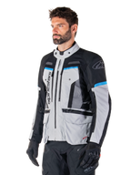 Alpinestars Bogota' Pro Drystar®-jakke, Ice Gray, sort og cyan, adventure-motorcykeljakke båret af en mand med sorte handsker, teknisk design med flere lommer og ventilationspaneler, high-performance køreudstyr