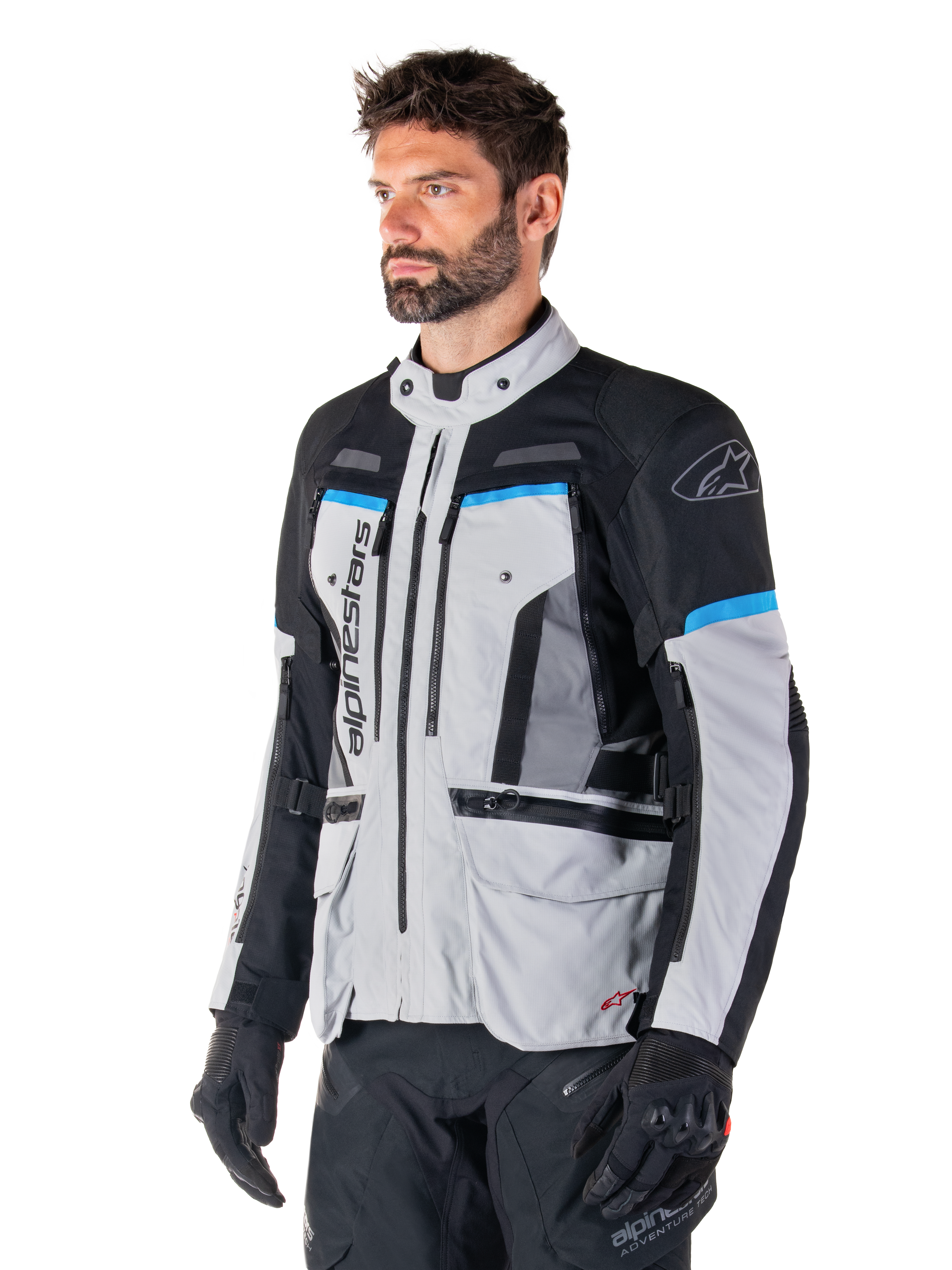 Alpinestars Bogota' Pro Drystar®-jakke, Ice Gray, sort og cyan, adventure-motorcykeljakke båret af en mand med sorte handsker, teknisk design med flere lommer og ventilationspaneler, high-performance køreudstyr