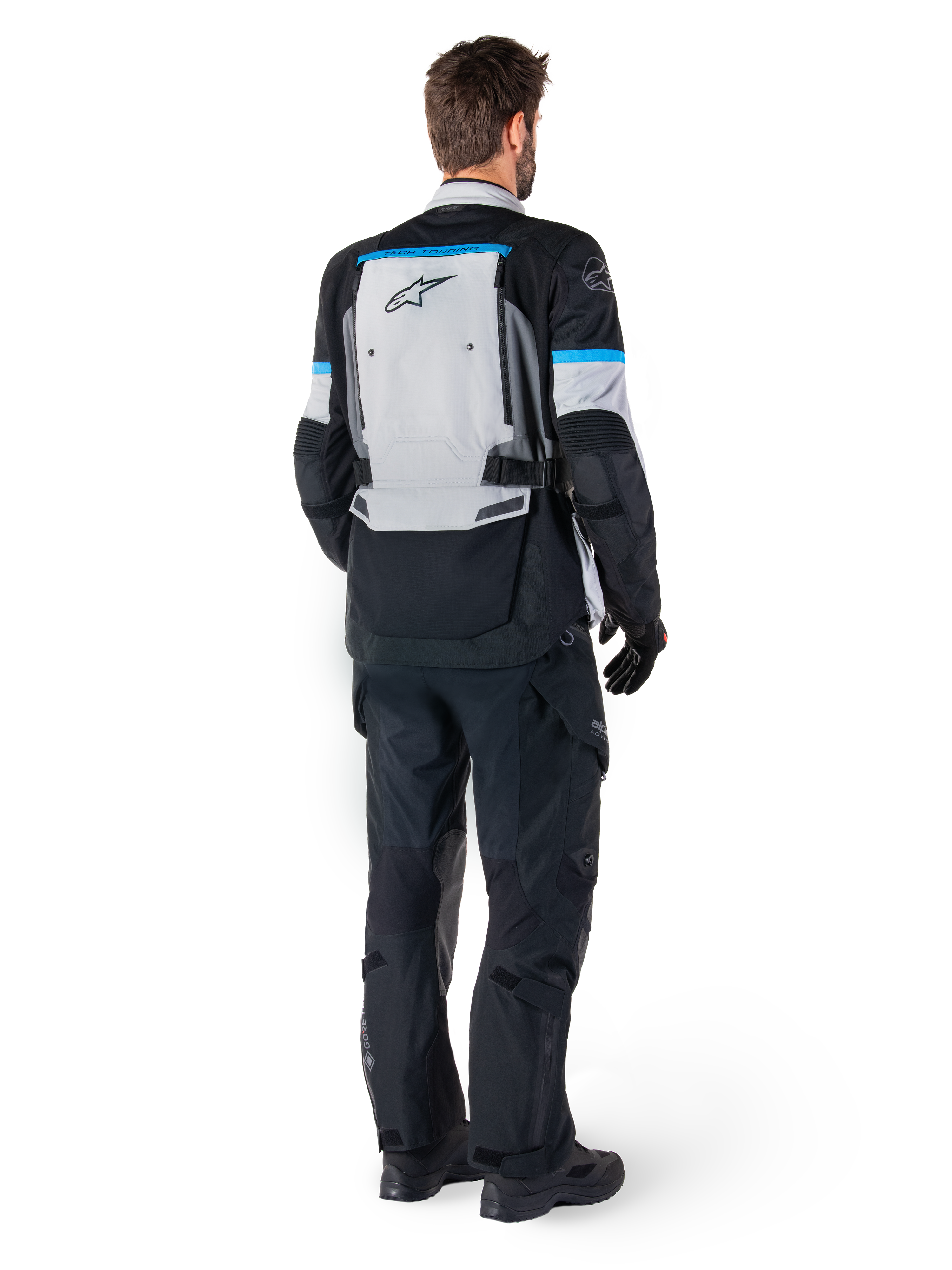 Alpinestars Bogota' Pro Drystar® jakke, adventure-motorcykeljakke, Ice Gray, sort og cyan, set bagfra, båret med matchende sorte bukser og handsker, med et stort gråt rygpanel, sort Alpinestars-logo og cyanblå accenter.