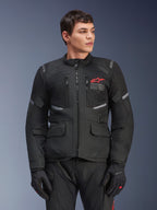 Alpinestars Andes Air Drystar® Jacket, Black Motorcycle Touring Jacket, Red Star Logo on Chest, featuring mesh ventilation panels and reflective accents, worn by male model with black riding gloves, dual-season adventure gear