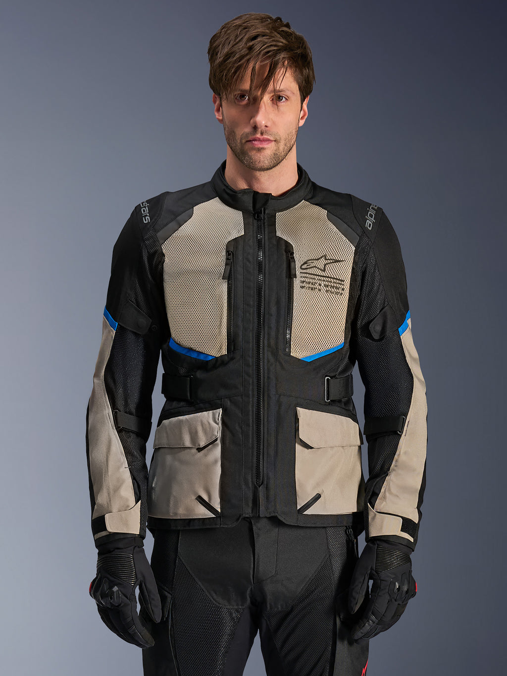 Alpinestars Andes Air Drystar-jakke, adventure touring-jakke, sort, laurel gray og klar blå, båret af en model med sorte handsker, med store mesh-paneler på brystet for luftgennemstrømning, cargo-lommer foran og blå detaljer, beskyttende motorcykel-touringudstyr