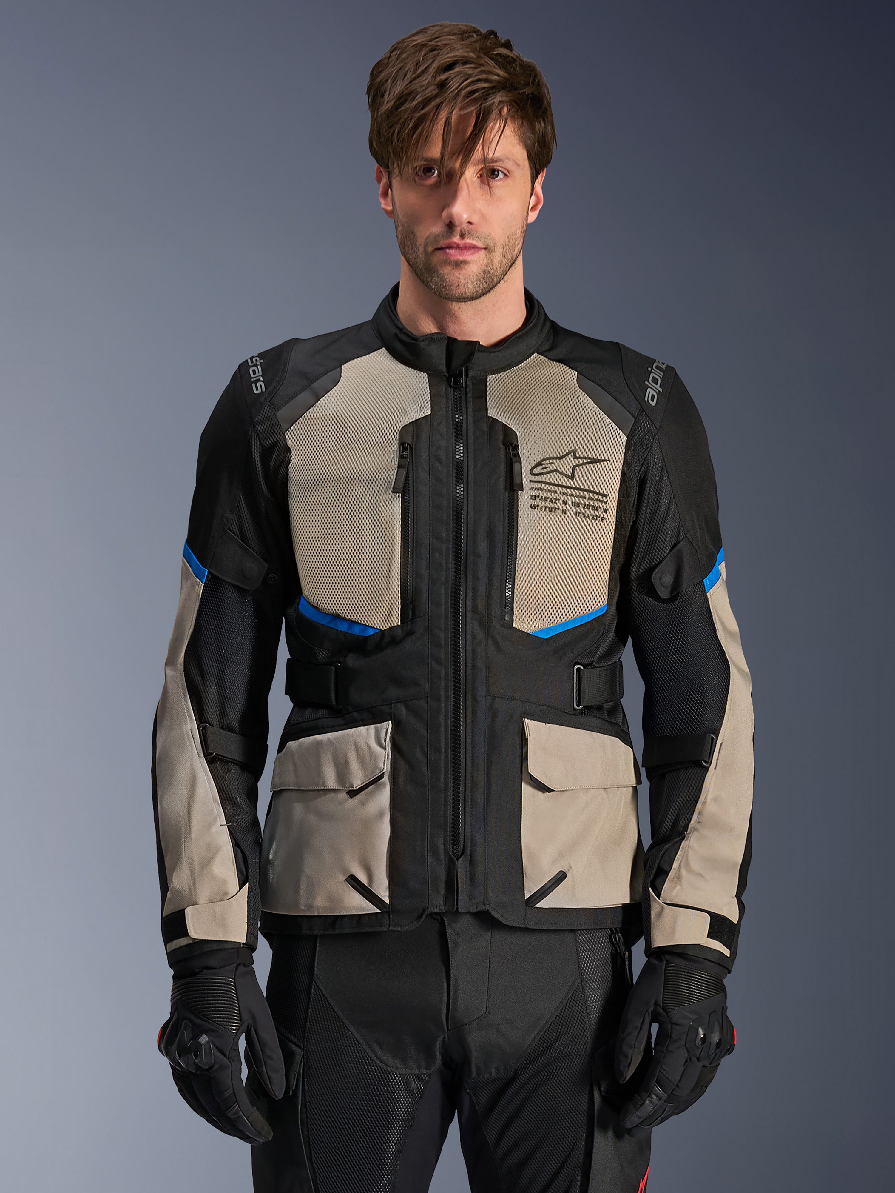 Alpinestars Andes Air Drystar-jakke, adventure touring-jakke, sort, laurel gray og klar blå, båret af en model med sorte handsker, med store mesh-paneler på brystet for luftgennemstrømning, cargo-lommer foran og blå detaljer, beskyttende motorcykel-touringudstyr
