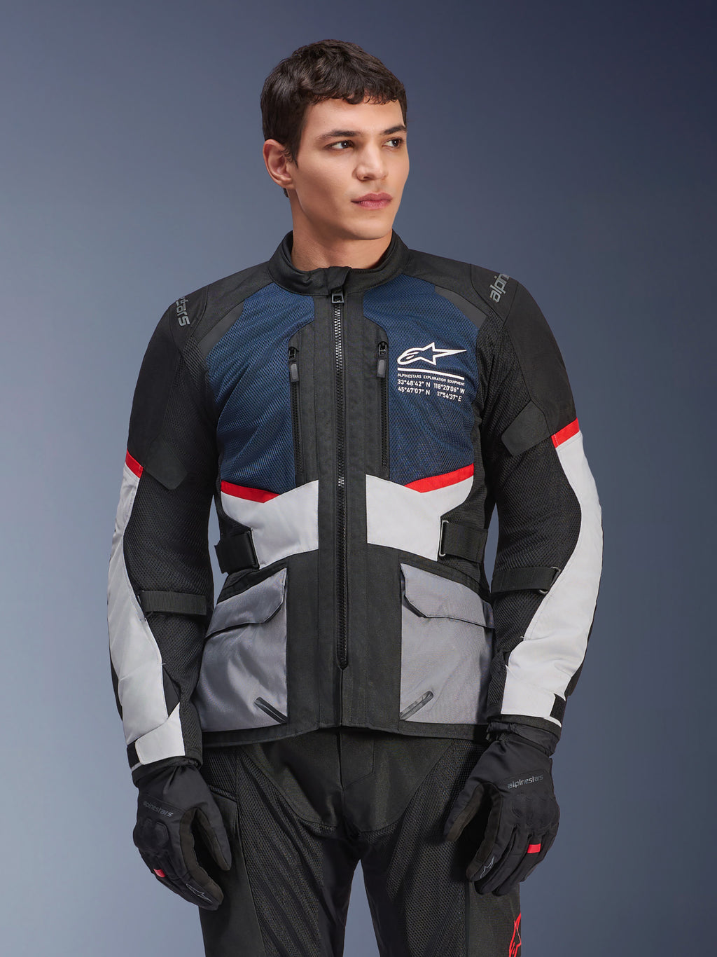 Alpinestars Andes Air Drystar®-jakke, motorcykel touringjakke, dyb blå, sort og isgrå med røde detaljer, båret af en mandlig model med sorte handsker, med mesh-ventilationspaneler og praktiske frontlommer, moderne udstyr til adventure- og landevejskørsel