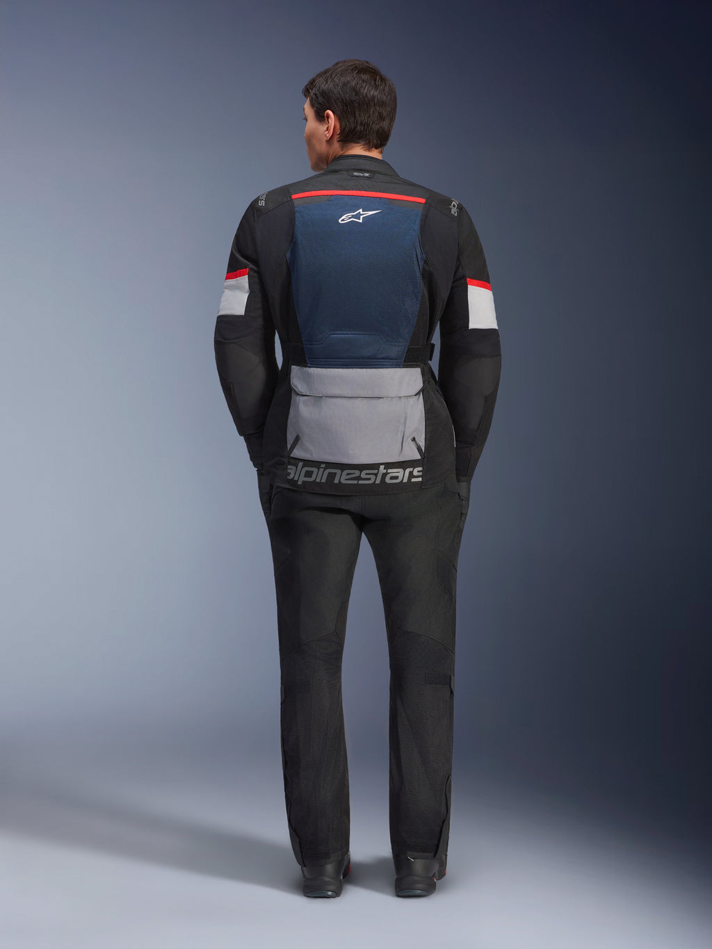 Alpinestars Andes Air Drystar-jakke, Deep Blue Black Ice Gray, set bagfra på model, med blåt mesh-rygpanel til ventilation, stor grå lomme forneden, røde og hvide detaljer på ærmerne, 'alpinestars' tekstlogo, kombineret med sorte motorcykelbukser for et komplet touring-outfit