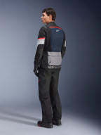 Mandlig model set skråt bagfra iført Alpinestars Andes Air Drystar®-jakke i Deep Blue Black Ice Gray, kombineret med sorte motorcykelbukser og handsker, med blåt mesh-rygpanel, grå utility-lomme på lænden og røde detaljer på ærmerne, professionelt adventure touring-udstyr.