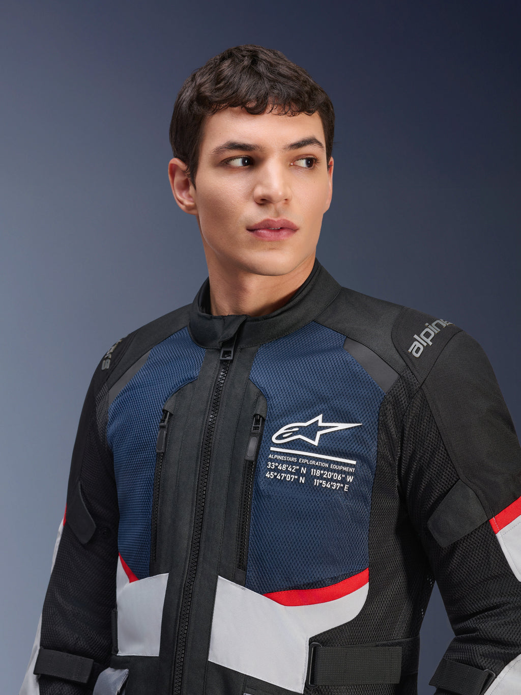 Alpinestars Andes Air Drystar® jakke, motorcykeljakke, Deep Blue Black og Ice Gray med røde detaljer, båret af mandlig model, med ventilerede brystpaneler i mesh, hvidt stjernelogo med udforskningskoordinater og vejklart adventure-design