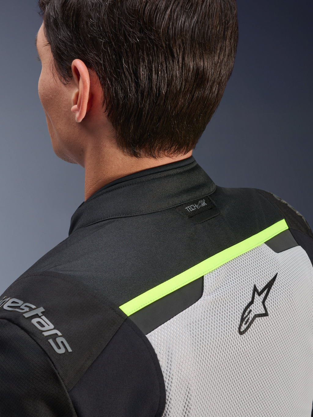 Alpinestars Andes Air Drystar® jakke, tekstil motorcykeljakke, Ice Gray, mørkegrå og sort, detalje af øverste ryg og skulder set bagfra, med åndbare mesh-paneler, fluorescerende gule detaljer og Tech-Air-logo på kraven.