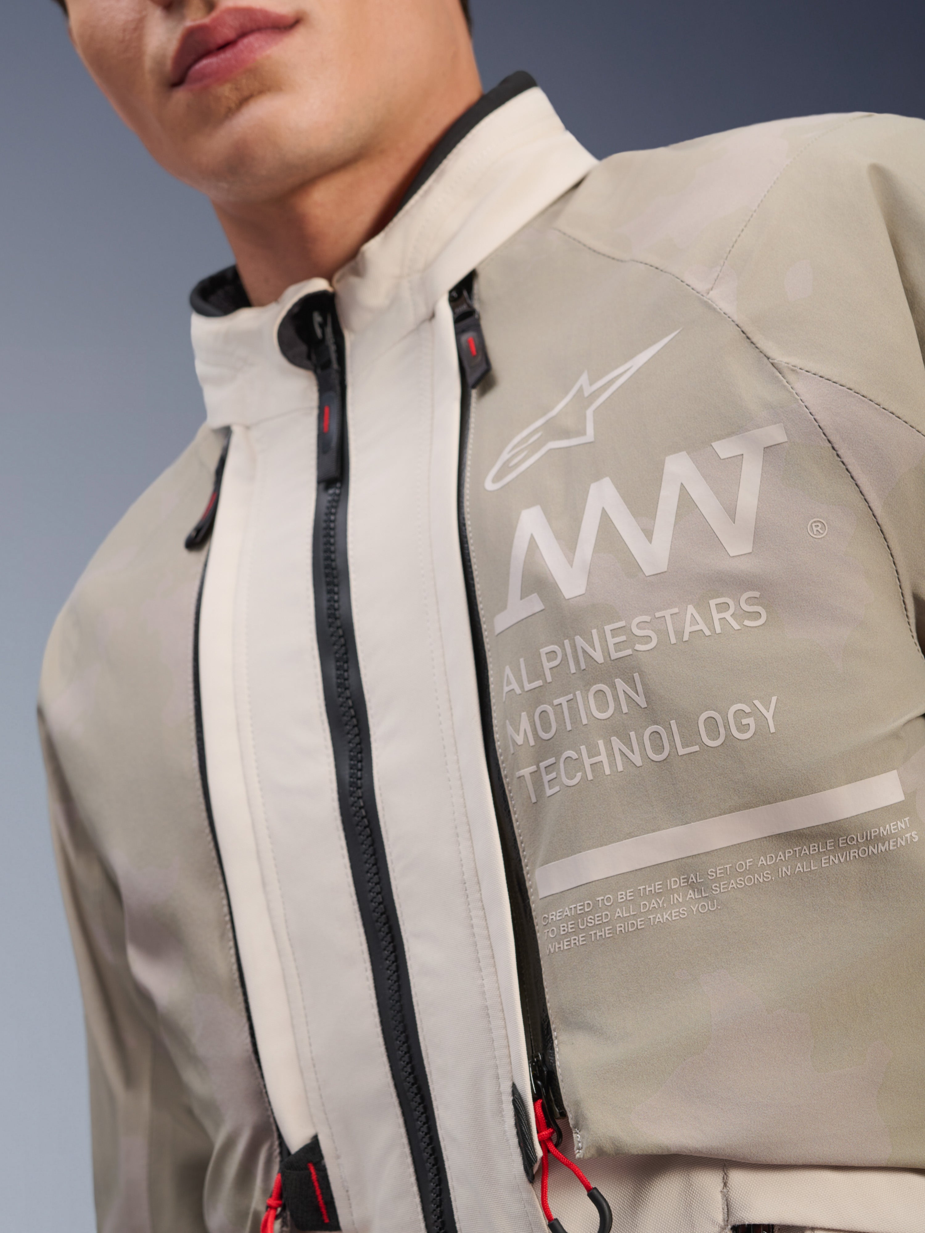 Alpinestars AMT-10LAB Drystar® XF jakke, White Sand Aluminum Camo, nærbillede af brystet med AMT Alpinestars Motion Technology branding, vandtætte lynlåse med røde snoretræk og tekstureret adventure-klar tekstil.