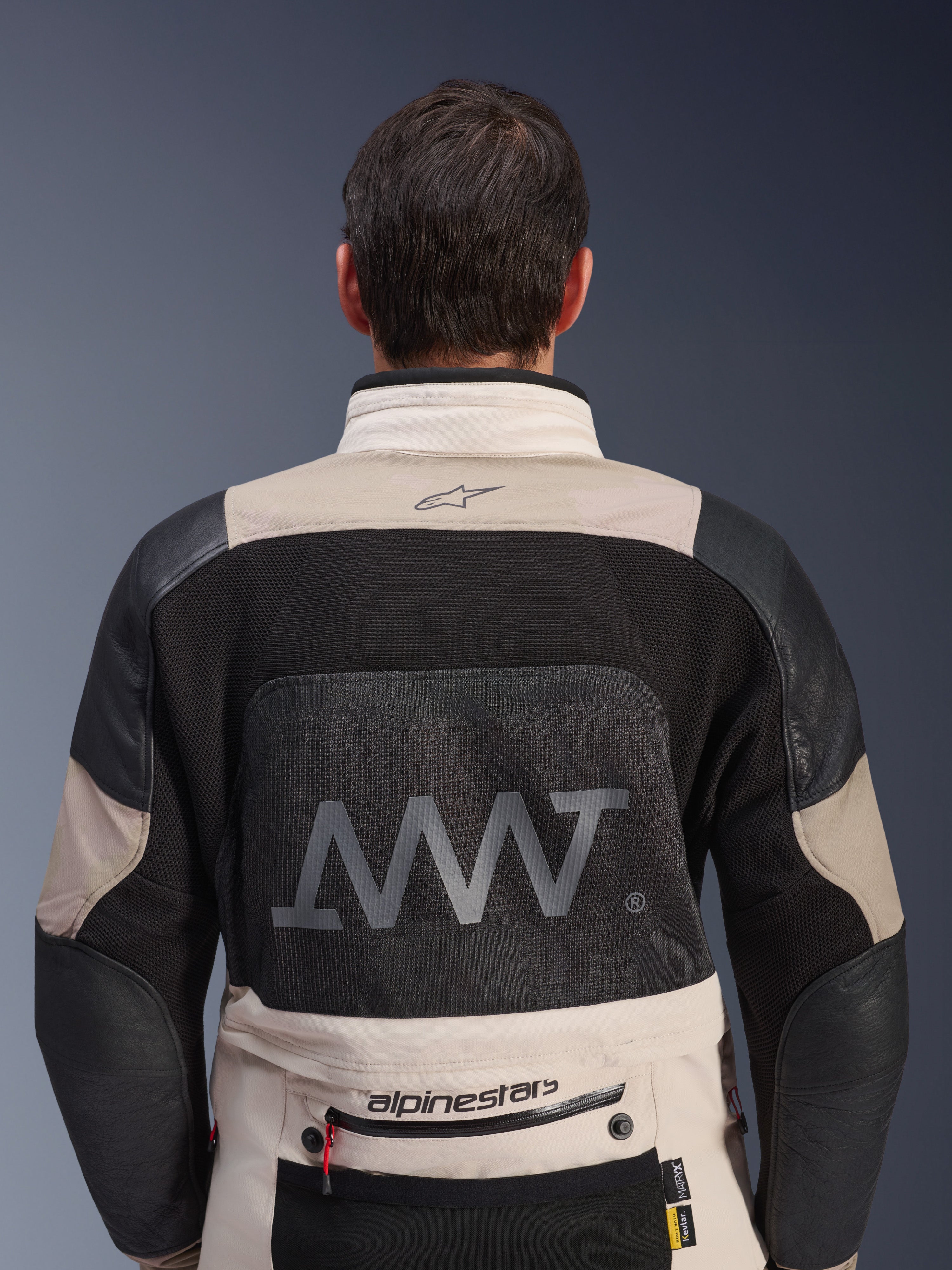 Bagfra-visning af Alpinestars AMT-10LAB Drystar® XF-jakke i White Sand og sort, med et stort AMT-logo på rygpanelet i mesh, Alpinestars-branding på den nederste del af ryggen og teknisk tekstilkonstruktion til adventure-motorcykelkørsel