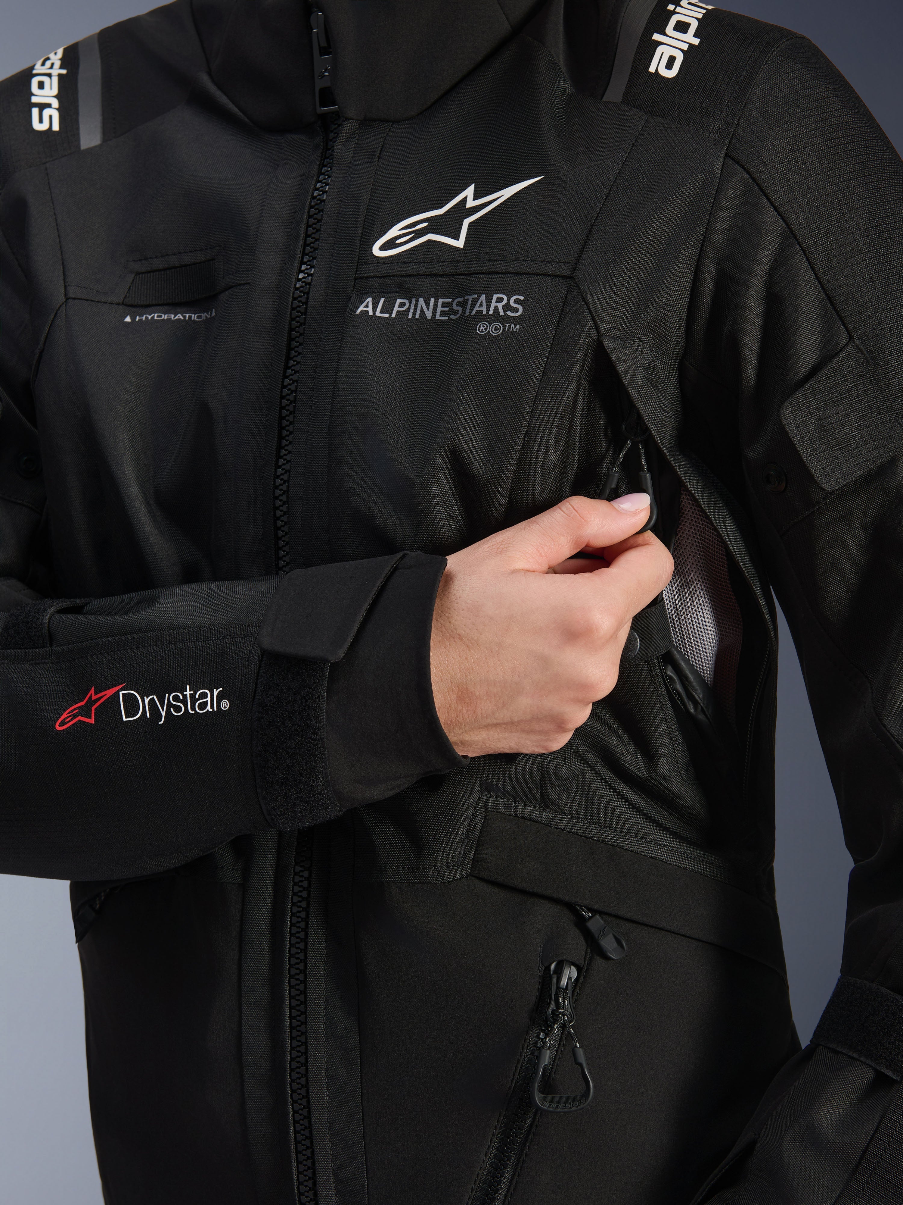Alpinestars Stella Andes V4 Drystar® jakke til kvinder, sort, detaljebillede der viser brystventilationsindtaget blive åbnet, med mesh-foring, Drystar®-logo på underarmen og løkke til hydreringsslange, teknisk motorcykelbeklædning.