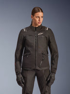 Alpinestars Stella Andes V4 Drystar-jakke, motorcykel-touringjakke til kvinder, sort, båret af en model med matchende kørebukser og handsker, med lynlåslukning foran, hvidt logo på brystet og Alpinestars-branding på skuldrene, elegant altvejrsudstyr.
