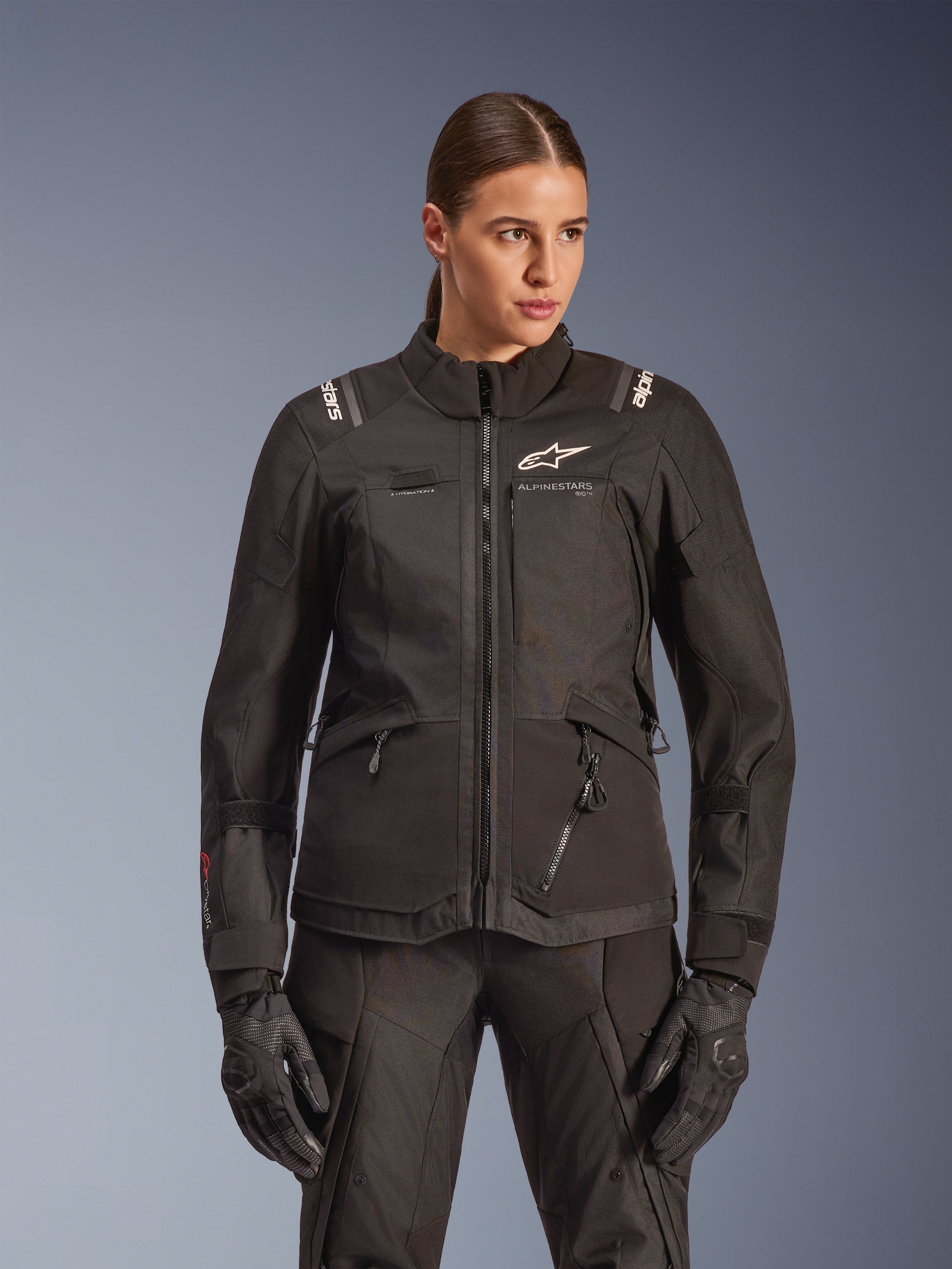 Alpinestars Stella Andes V4 Drystar-jakke, motorcykel-touringjakke til kvinder, sort, båret af en model med matchende kørebukser og handsker, med lynlåslukning foran, hvidt logo på brystet og Alpinestars-branding på skuldrene, elegant altvejrsudstyr.