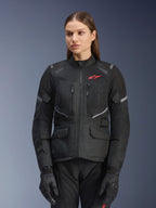 Alpinestars Stella Andes Air Drystar Jacket, Women's Motorcycle Touring Jacket, Black with gray accents and a small red logo, featuring mesh ventilation panels, a high collar, and multiple utility pockets, worn with matching riding gloves and pants