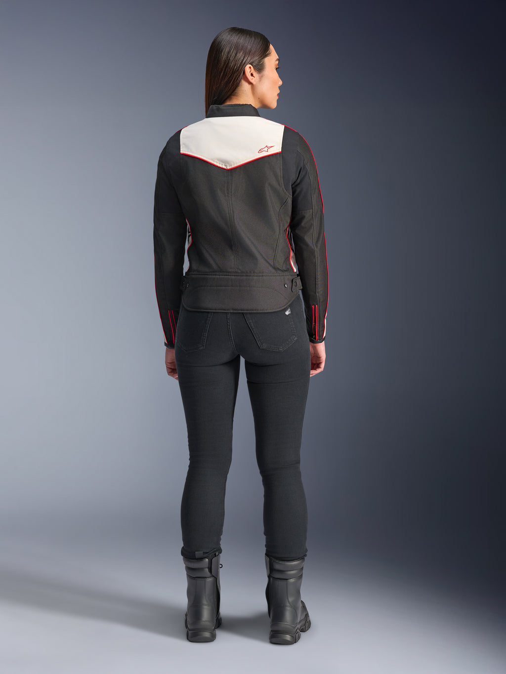 Bagfra set af en kvindelig model iført Alpinestars Stella T-Dyno WR-jakken i Black Ecru Bright Red, med et fremtrædende cremefarvet rygpanel og røde logo-detaljer, stylet med sorte bukser og støvler, en vintage-inspireret tekstil-motorcykeljakke.