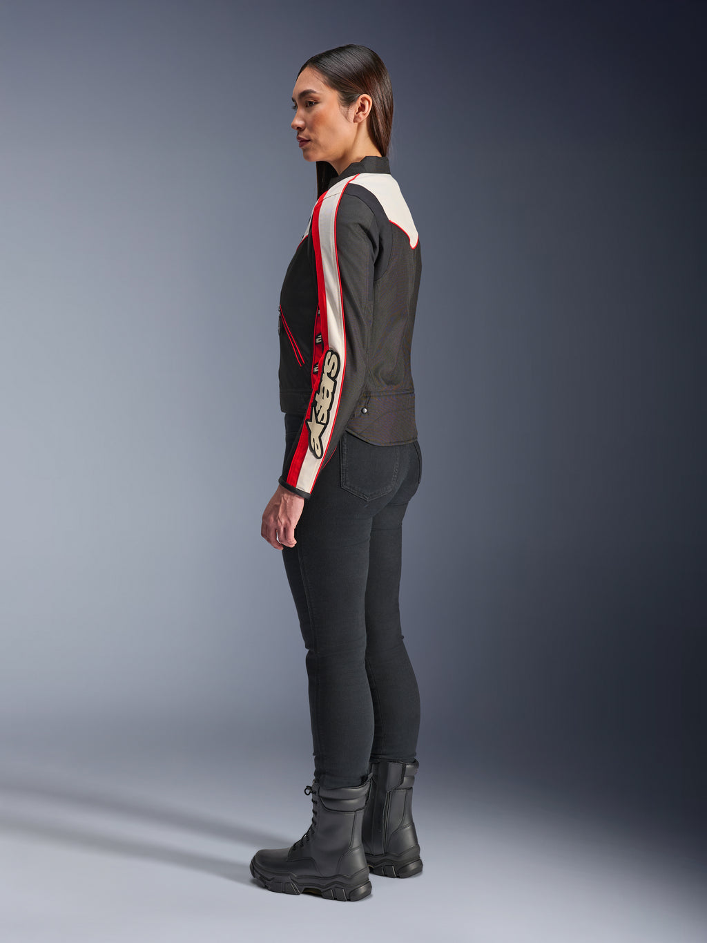 Alpinestars Stella T-Dyno WR Jakke, tekstilmotorcykeljakke til kvinder, sort, ecru og lys rød, med vintage-inspireret design og Astars-branding på ærmet, båret med tætsiddende sorte bukser og sorte støvler, kortere biker-pasform til urban kørsel