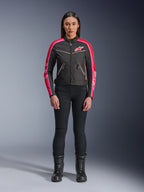 Kvinde iført Alpinestars Stella T-Dyno WR-jakke, sort med klare røde og fuchsia-farvede detaljer, tekstiljakke i vintage-stil med lyserødt logo og striber på ærmerne, kombineret med sorte bukser og snørestøvler, urbant motorcykeludstyr