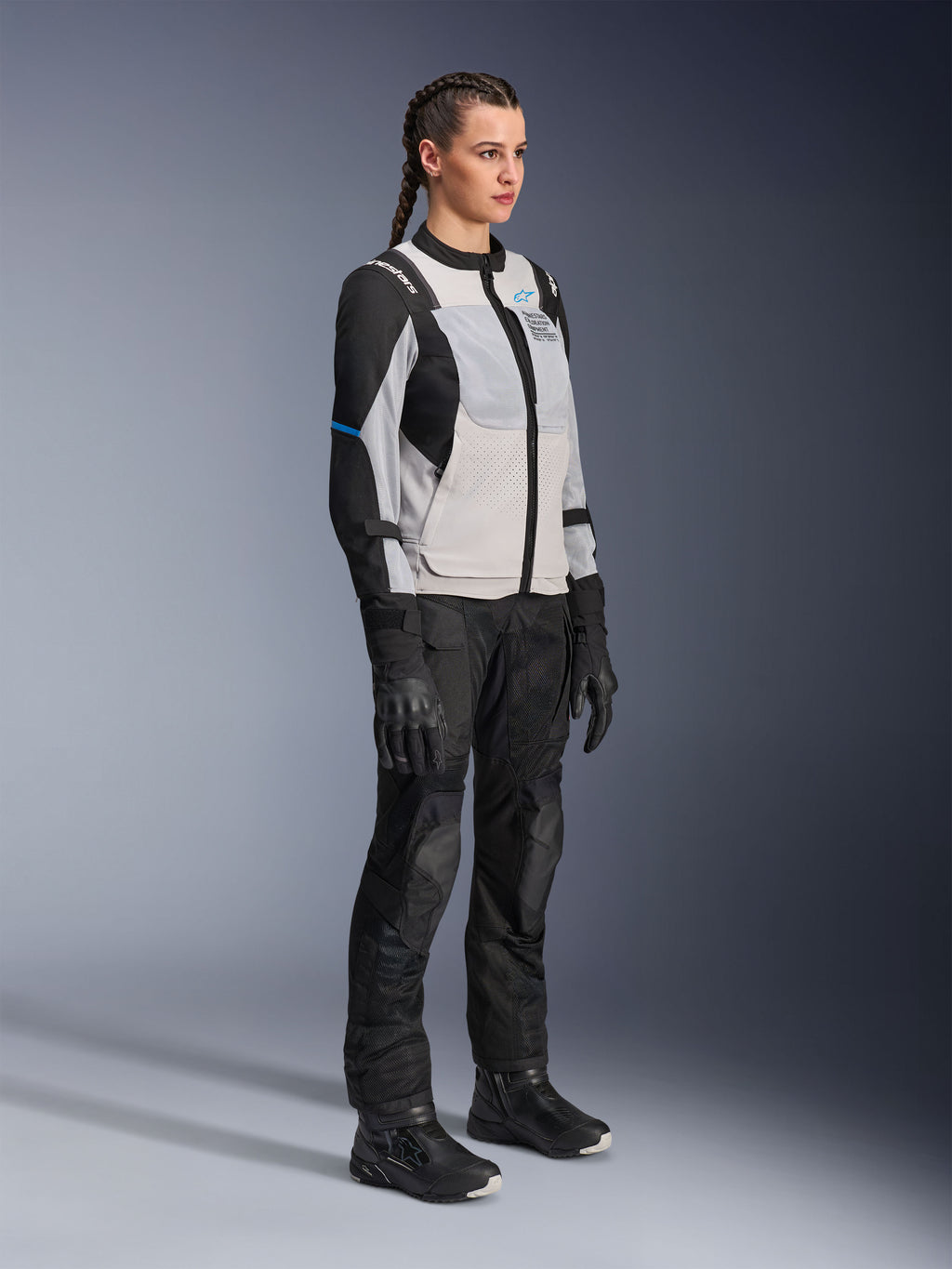 Model iført Alpinestars Stella ST-2 Air-jakke i Ice Gray og Black, teknisk motorcykeljakke til kvinder med mesh-paneler og softshell-konstruktion, kombineret med sorte adventure touring-bukser og støvler, med blå detaljer og et moderne køredesign