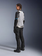 Kvindelig motorcyklist iført Alpinestars Stella ST-2 Air-jakke i Ice Gray og sort, set bagfra i trekvart profil, der fremhæver det store lysegrå mesh-rygpanel, sorte ærmer med en blå accentstribe og et blåt Alpinestars-logo, kombineret med sorte motorcykelbukser, handsker og støvler for et komplet adventure touring-outfit.