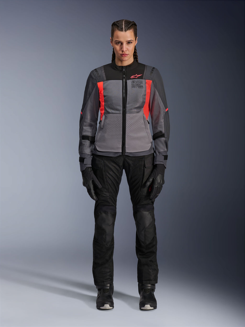 Kvinde iført Alpinestars Stella ST-2 Air-jakke i Deep Gray, Dark Gray og Fluo Coral, kombineret med sorte motorcykelbukser og handsker, set forfra, moderne mesh adventure-touringudstyr til kvinder