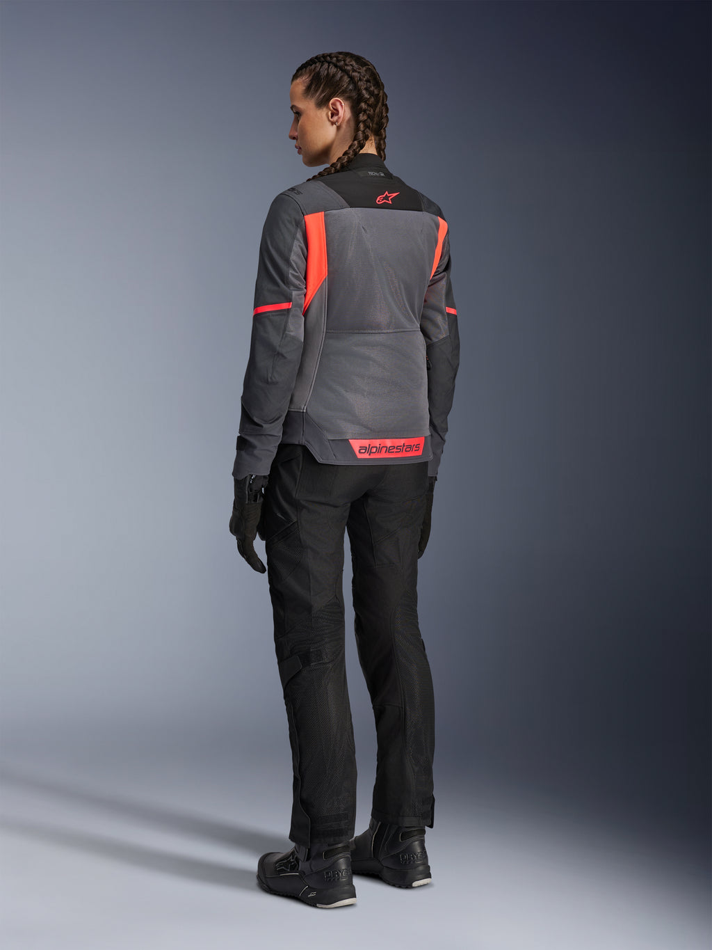 Kvinde iført Alpinestars Stella St-2 Air-jakke, motorcykel touring-jakke, Deep Gray og Dark Gray med Fluo Coral-detaljer, stylet med sorte kørebukser og handsker, set bagfra med store mesh-paneler og reflekterende coral-branding, designet til sommerens køreoplevelser