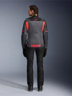 Rygbillede af en model iført Alpinestars Woman Stella St-2 Air Jacket i Deep Gray og Dark Gray med Fluo Coral-detaljer, med store mesh-ventilationspaneler på ryggen og reflekterende logodetaljer, kombineret med sorte motorcykelbukser og -handsker.